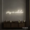 Stay Awhile neon sign in neutral white for cozy cafes, home decor, and hospitality settings.