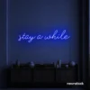 Stay Awhile neon sign in dark blue for cozy cafes, home decor, and hospitality settings.