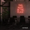 This Must Be The Place neon sign in peachy pink for cozy salons, boutique shops, and cafe decor.